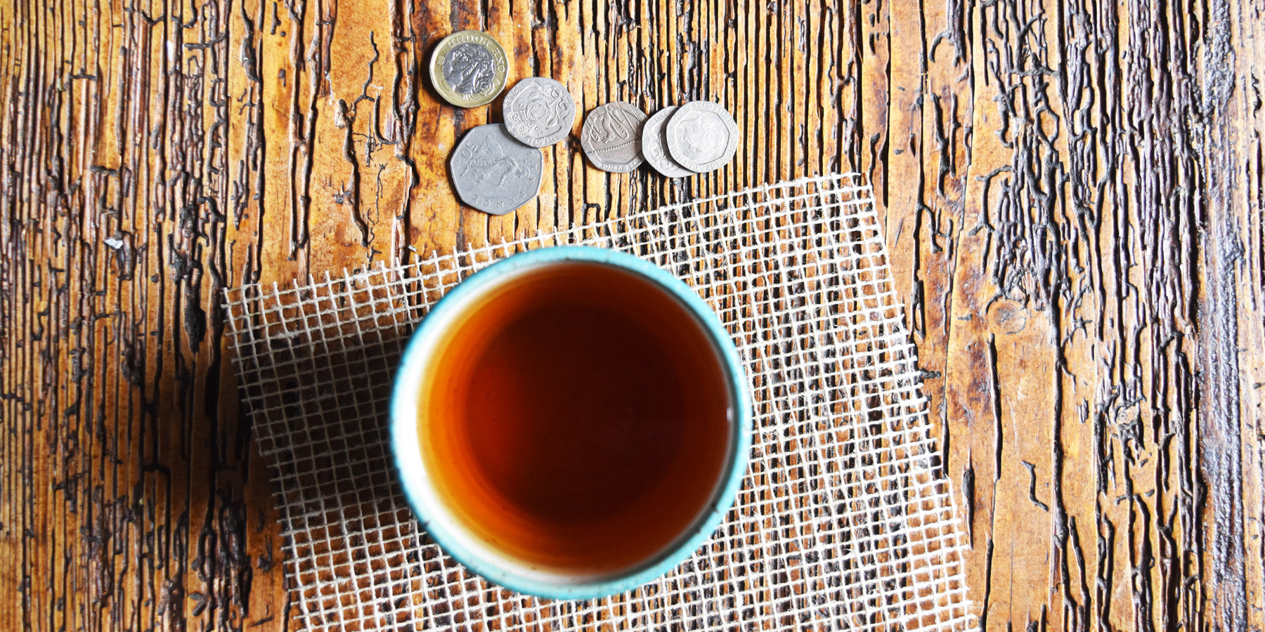 a cup of tea on a wooden table with some pennies beside it