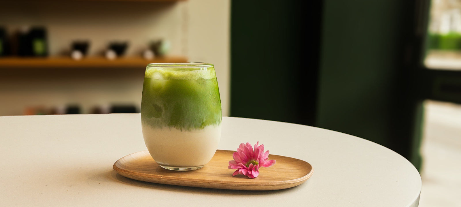 A glass of matcha and a pink flower on a wooded tray
